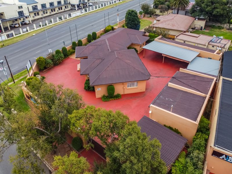 Aerial view of a commercial property featuring a main building with a metal roof, extensive paved parking area, and covered carport facilities.