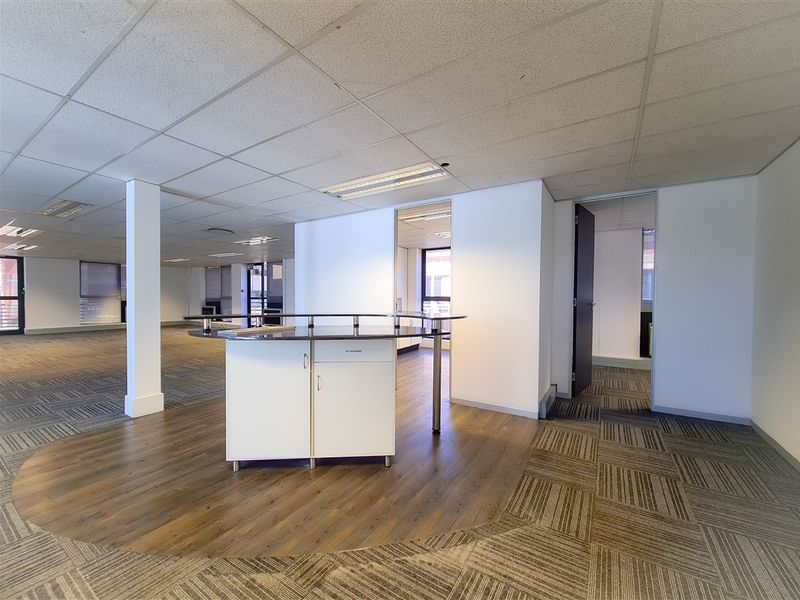 Spacious open-plan office area featuring a central built-in reception desk, suspended ceilings, and a mix of carpet and laminate flooring.