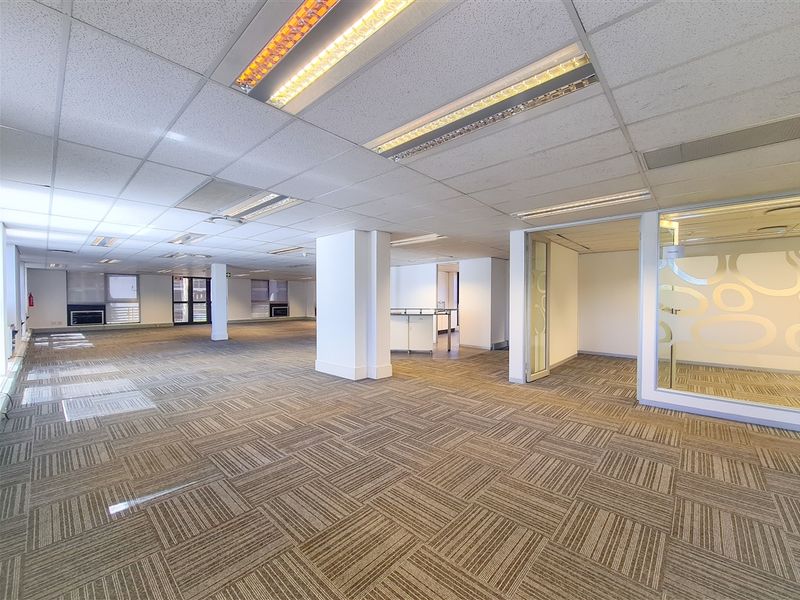 Spacious open-plan office area featuring suspended ceilings, recessed lighting, carpet tiles, and glass-partitioned private office spaces.