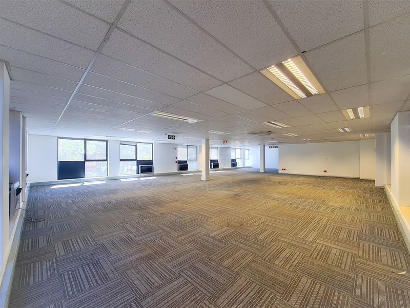 A spacious, open-plan office area featuring suspended ceilings, recessed lighting, and large windows providing ample natural light.