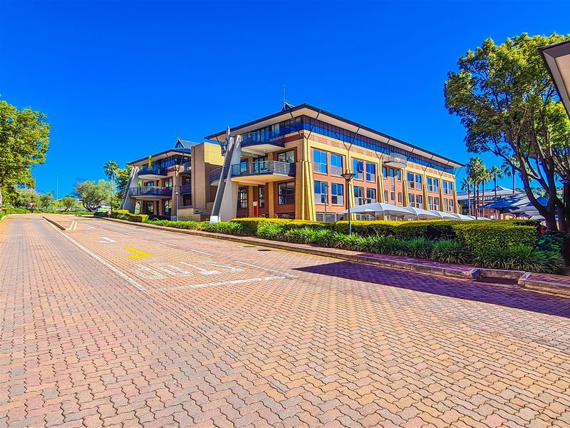 A view of a multi-story office building featuring brick paving, landscaped hedges, and balconies, showcasing the property's exterior facade and approach.