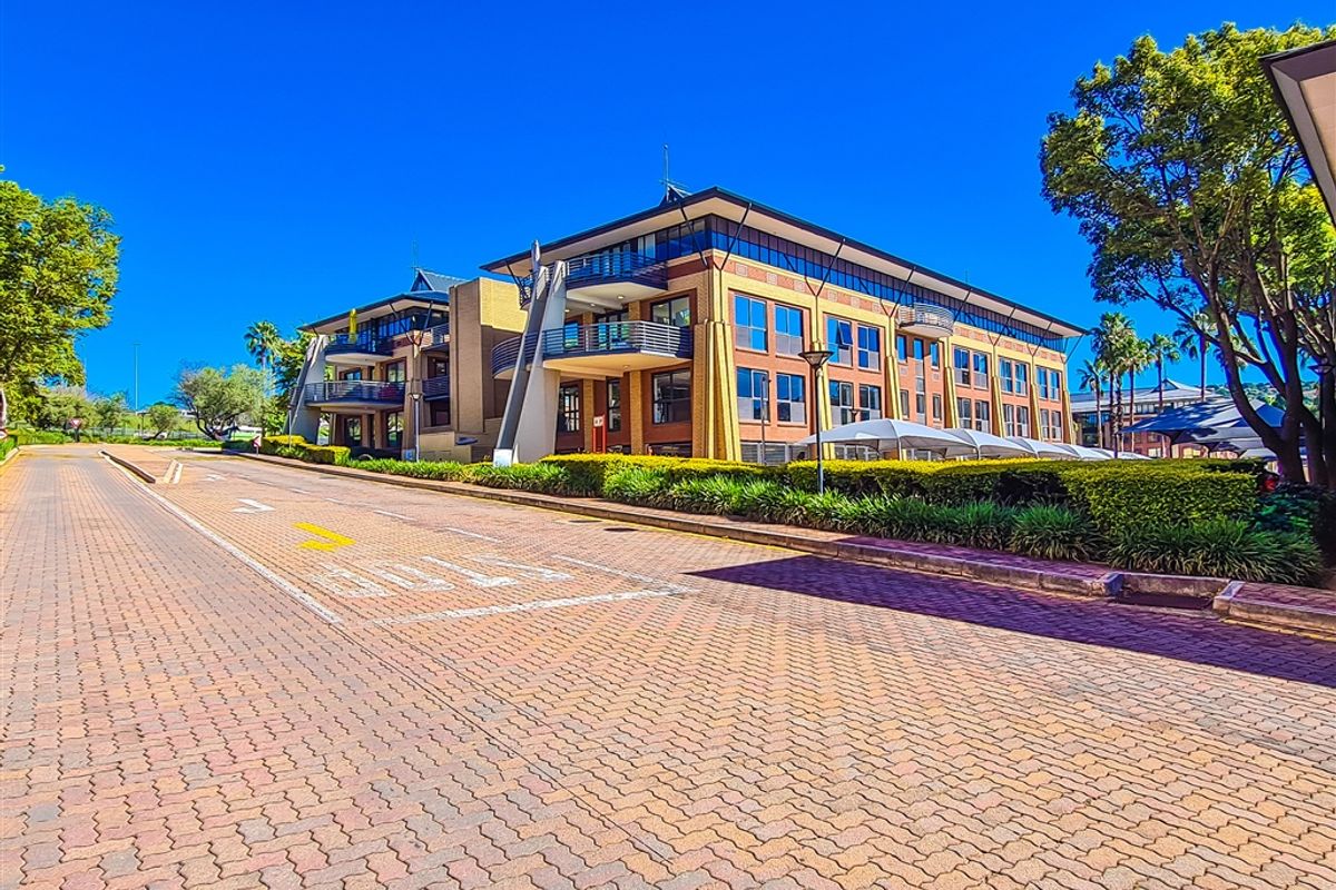 A view of a multi-story office building featuring brick paving, landscaped hedges, and balconies, showcasing the property's exterior facade and approach.