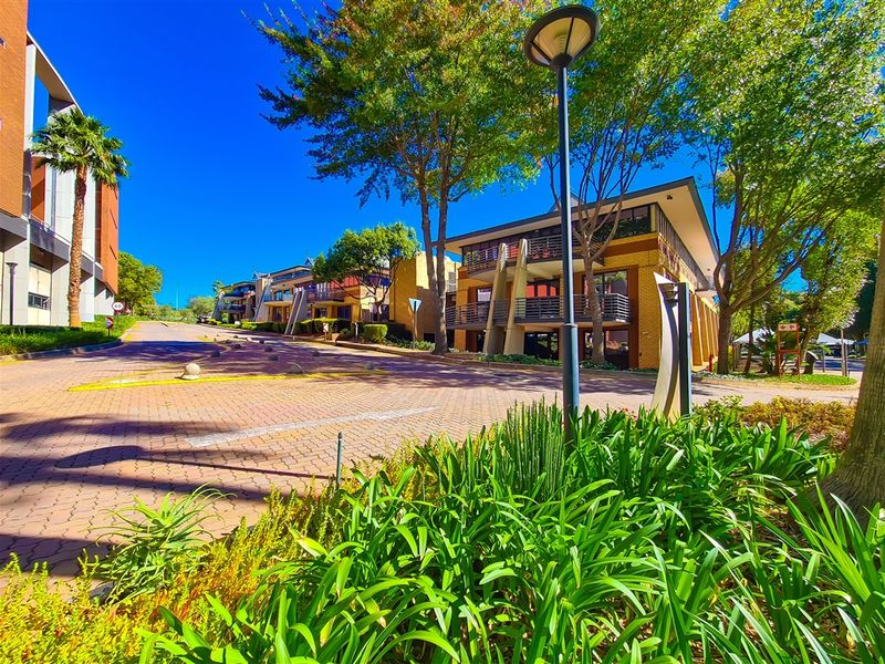 A view of the office park entrance featuring paved driveways, landscaped gardens, and multi-story commercial buildings with balconies.