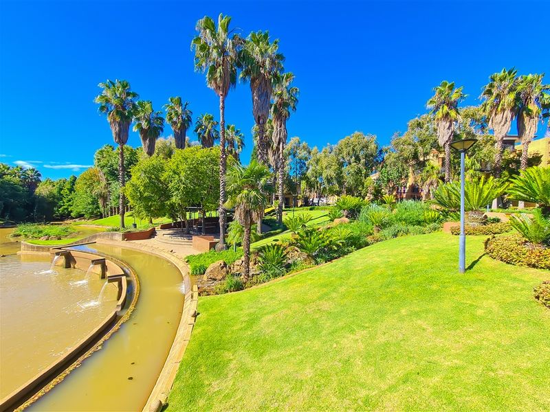 A well-maintained landscaped garden area featuring mature palm trees, manicured lawns, and a decorative water feature.