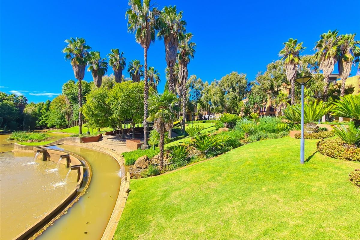 A well-maintained landscaped garden area featuring mature palm trees, manicured lawns, and a decorative water feature.