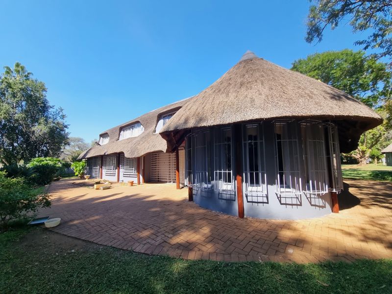 Rear view of a farm-style residence featuring a traditional thatched roof, brick paved patio area, and secure window treatments.