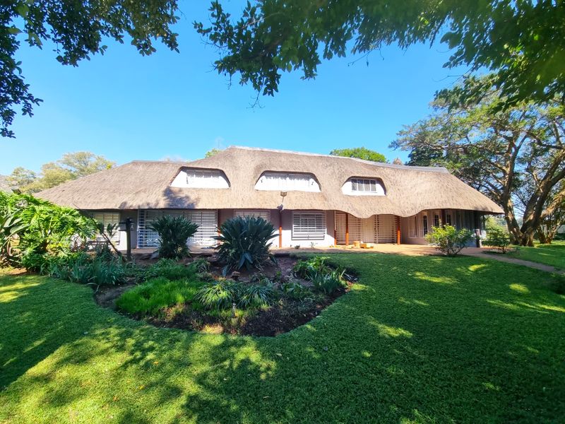 A well-maintained farm-style residence featuring a traditional thatched roof, dormer windows, and secure shutters, set within a lush, established garden.