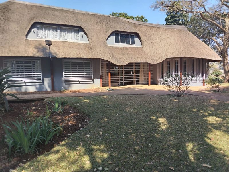 Rear view of a farm-style residence featuring a traditional thatch roof, security bars on windows, and a paved patio area overlooking the garden.