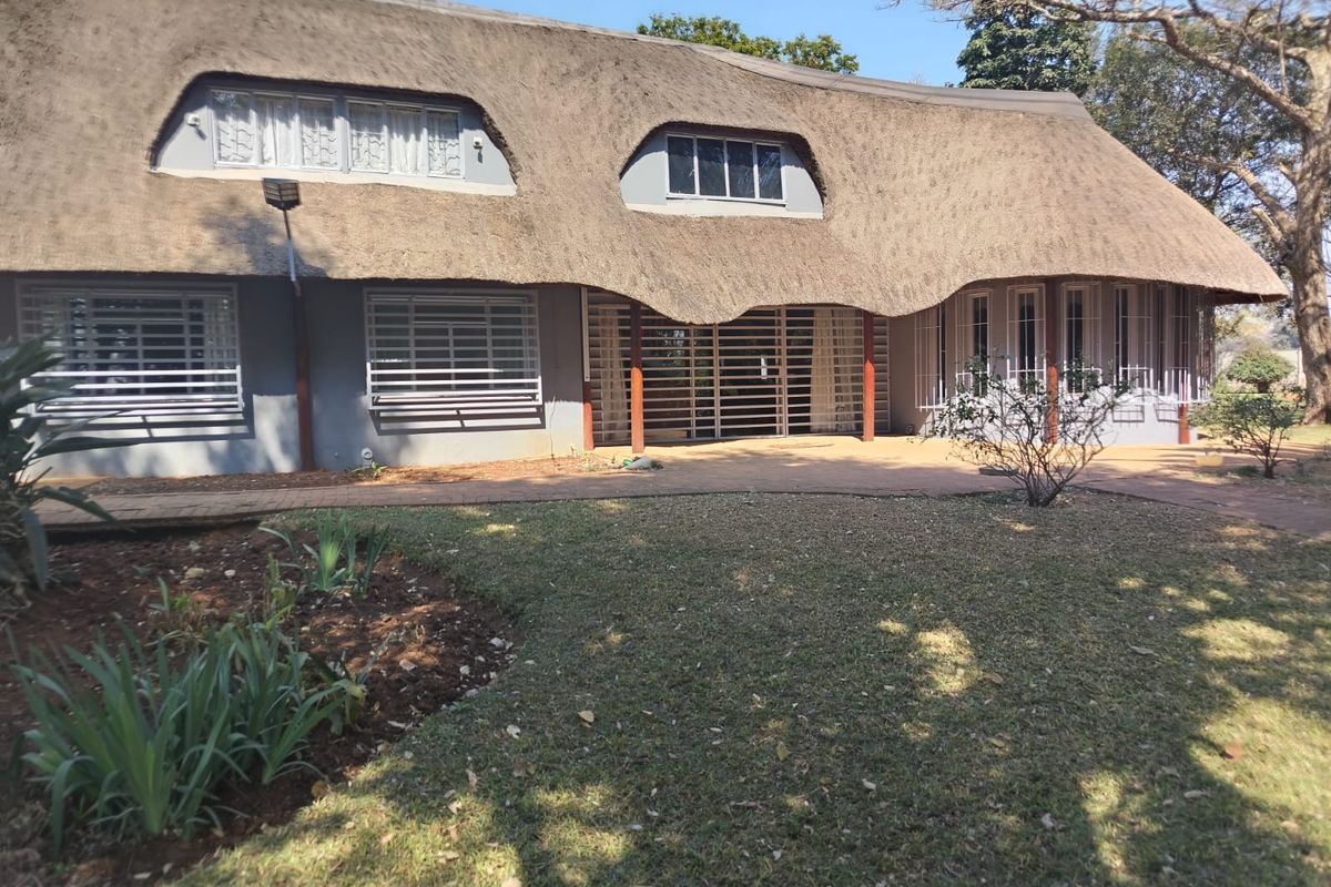 Rear view of a farm-style residence featuring a traditional thatch roof, security bars on windows, and a paved patio area overlooking the garden.
