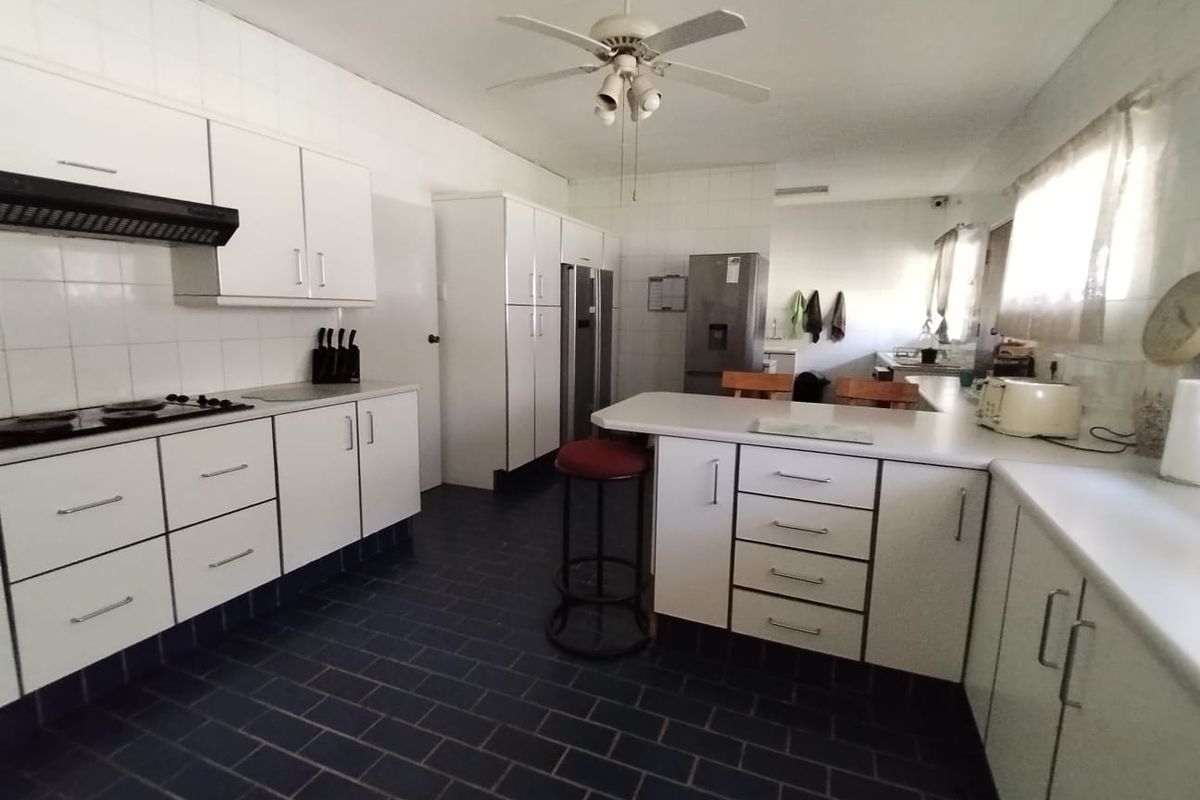 A functional kitchen featuring white built-in cabinetry, a breakfast counter, dark tiled flooring, and a ceiling fan, offering a clean but dated aesthetic.