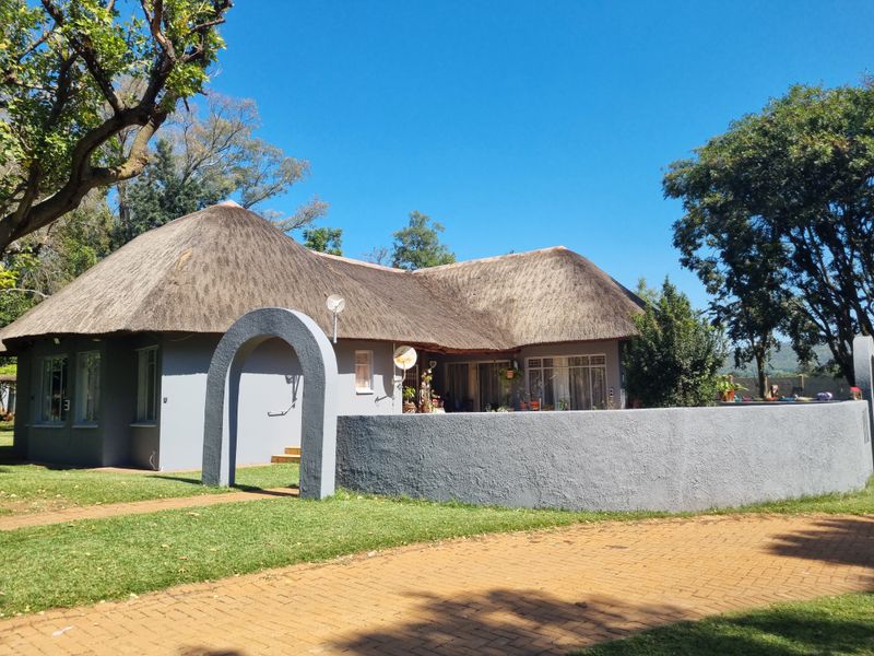 A charming farmhouse featuring a traditional thatched roof, a curved masonry boundary wall, and a paved driveway entrance.
