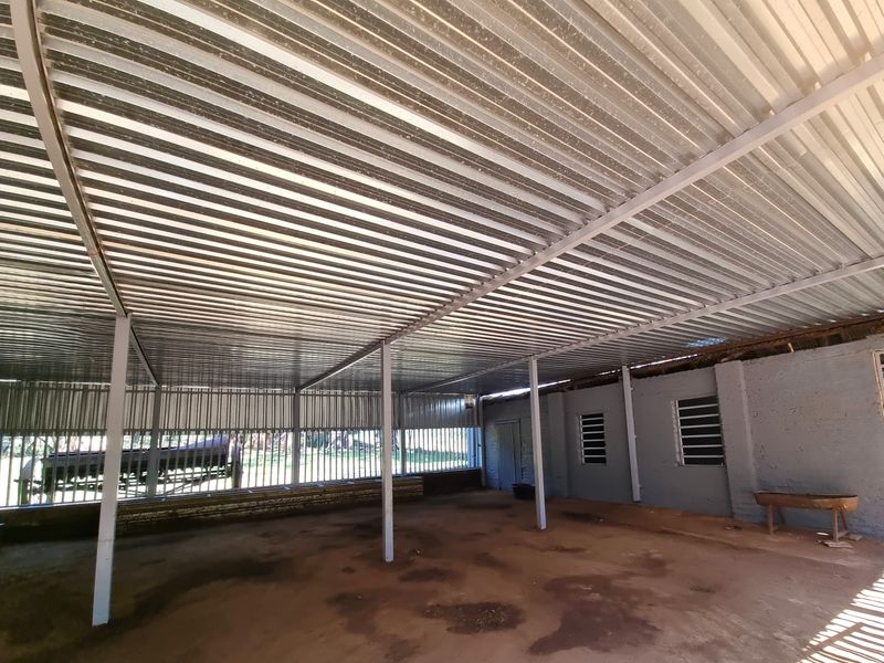 A large, open-sided utility or storage structure featuring a corrugated metal roof, steel support columns, and secure metal bar fencing.