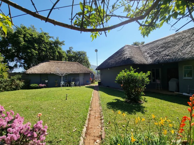 A well-maintained rear garden area featuring two structures with traditional thatch roofs, connected by a central brick paved pathway.