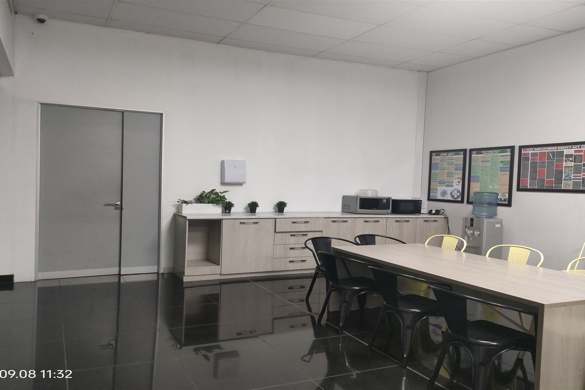 A functional industrial kitchen or breakroom area featuring built-in cabinetry, dark tiled flooring, and a suspended ceiling.