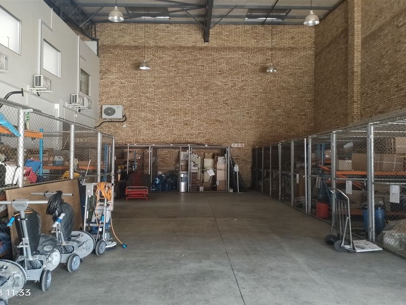 Industrial utility space featuring high ceilings with exposed steel trusses, brick walls, concrete flooring, and multiple chain-link storage partitions.