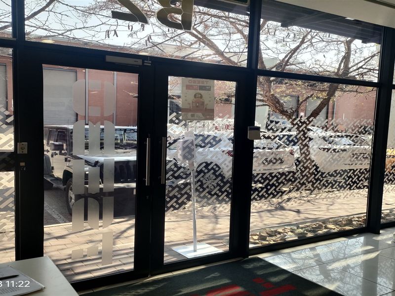 Modern industrial entrance area featuring large floor-to-ceiling glass panels and aluminium framed doors, providing clear views of the exterior parking area.