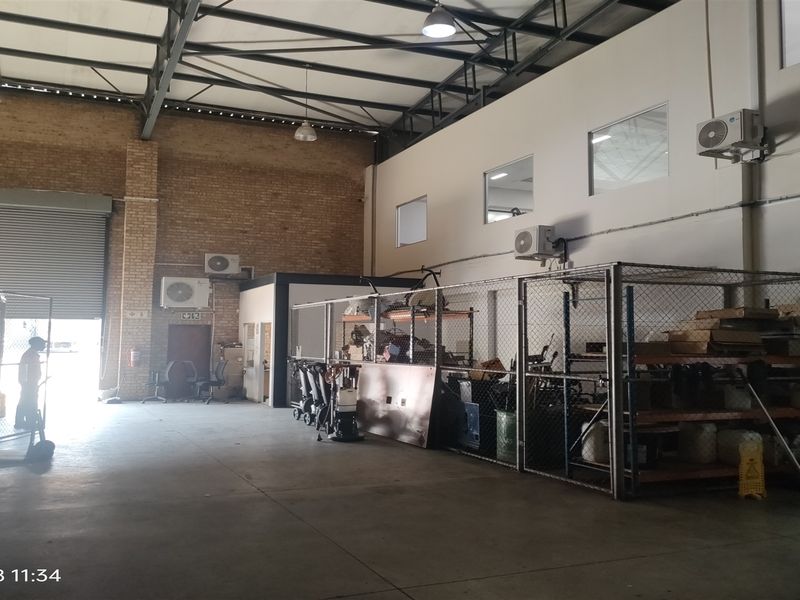 Industrial warehouse space featuring exposed steel trusses, concrete flooring, brick wall accents, and secure chain-link partitioned storage areas with wall-mounted air conditioning units.