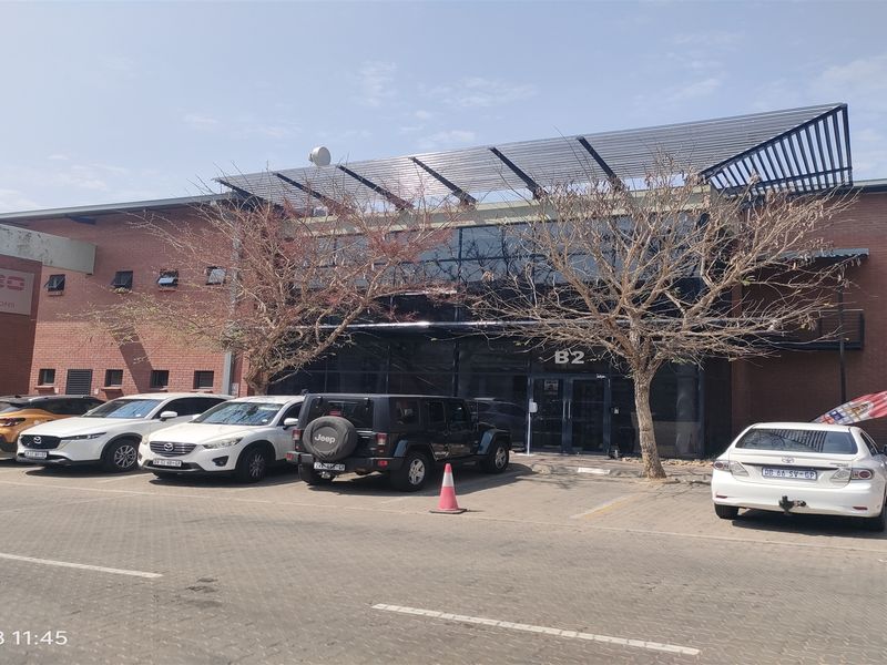 Front exterior view of an industrial office building featuring a brick facade, glass curtain wall entrance, and dedicated paved parking area.