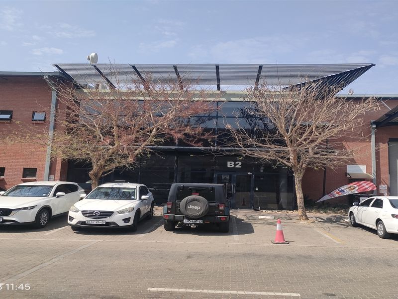 Front elevation of an industrial unit featuring a brick facade, glass curtain wall entrance, and paved parking area.