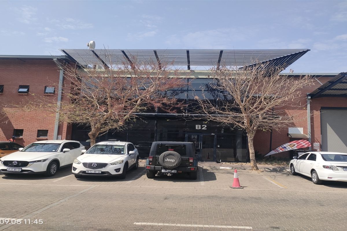 Front elevation of an industrial unit featuring a brick facade, glass curtain wall entrance, and paved parking area.