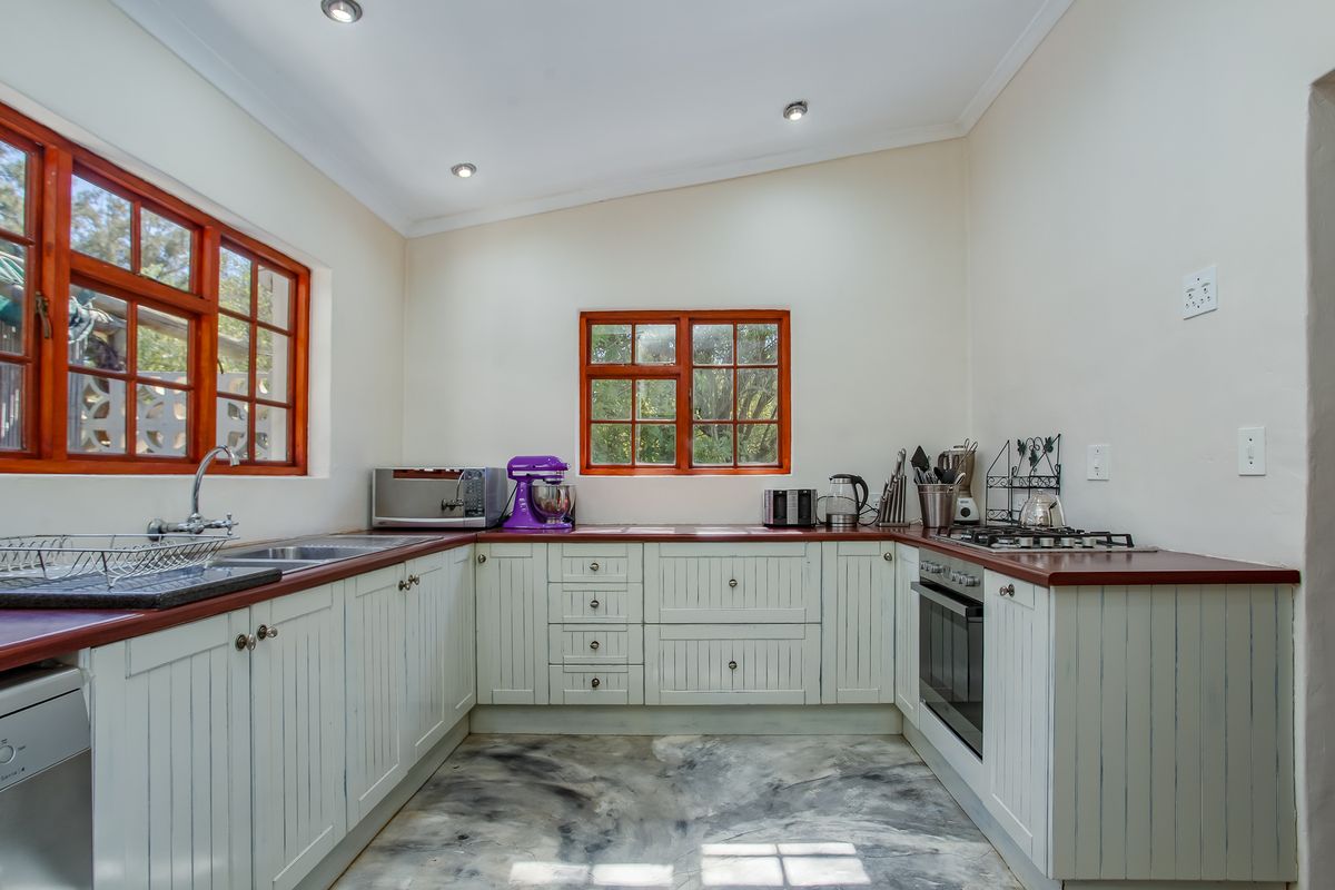 A functional kitchen featuring white cabinetry, dark countertops, a built-in oven, gas hob, and large windows providing natural light.