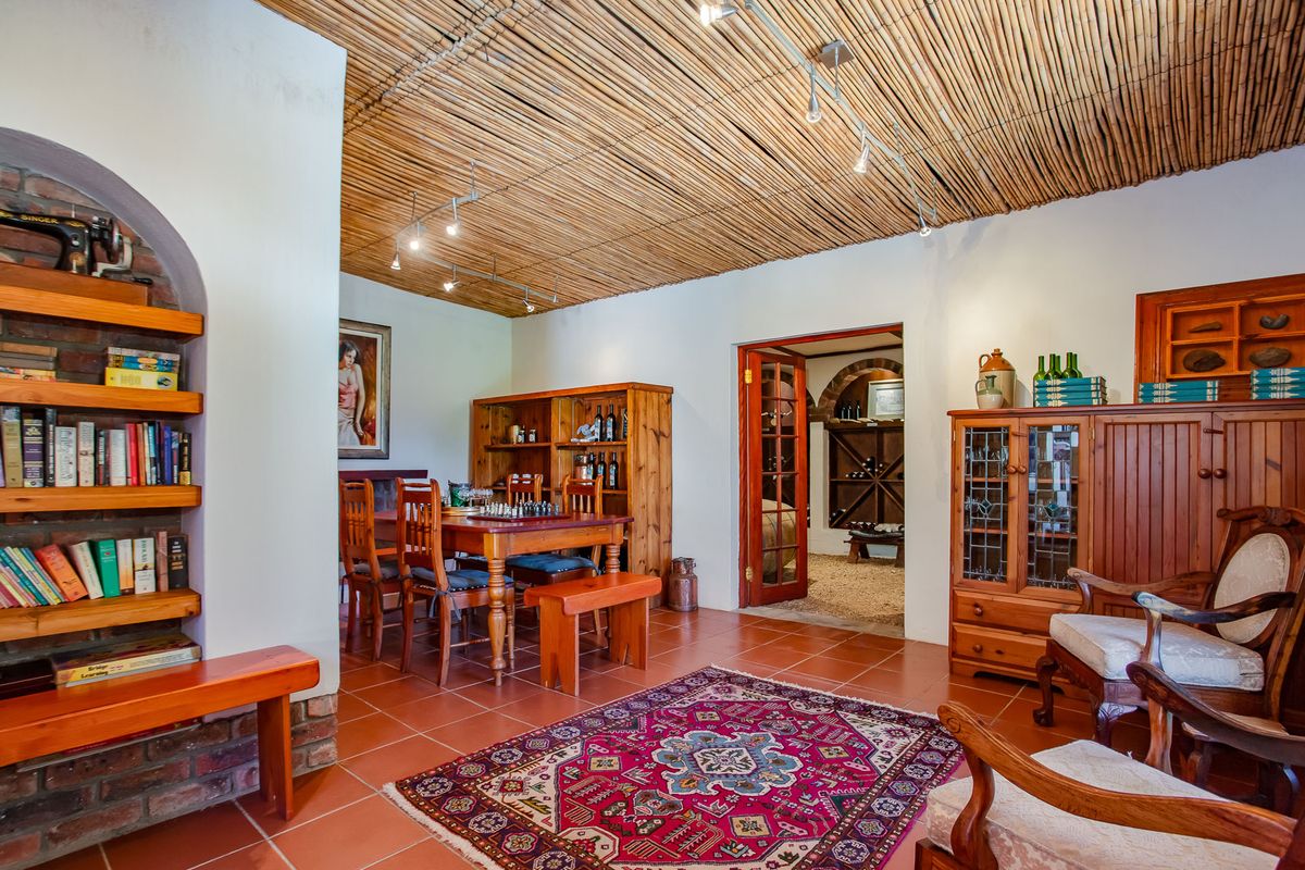 A rustic living area featuring a unique reed ceiling, terracotta floor tiles, and a built-in brick bookshelf, with an adjacent wine cellar visible.