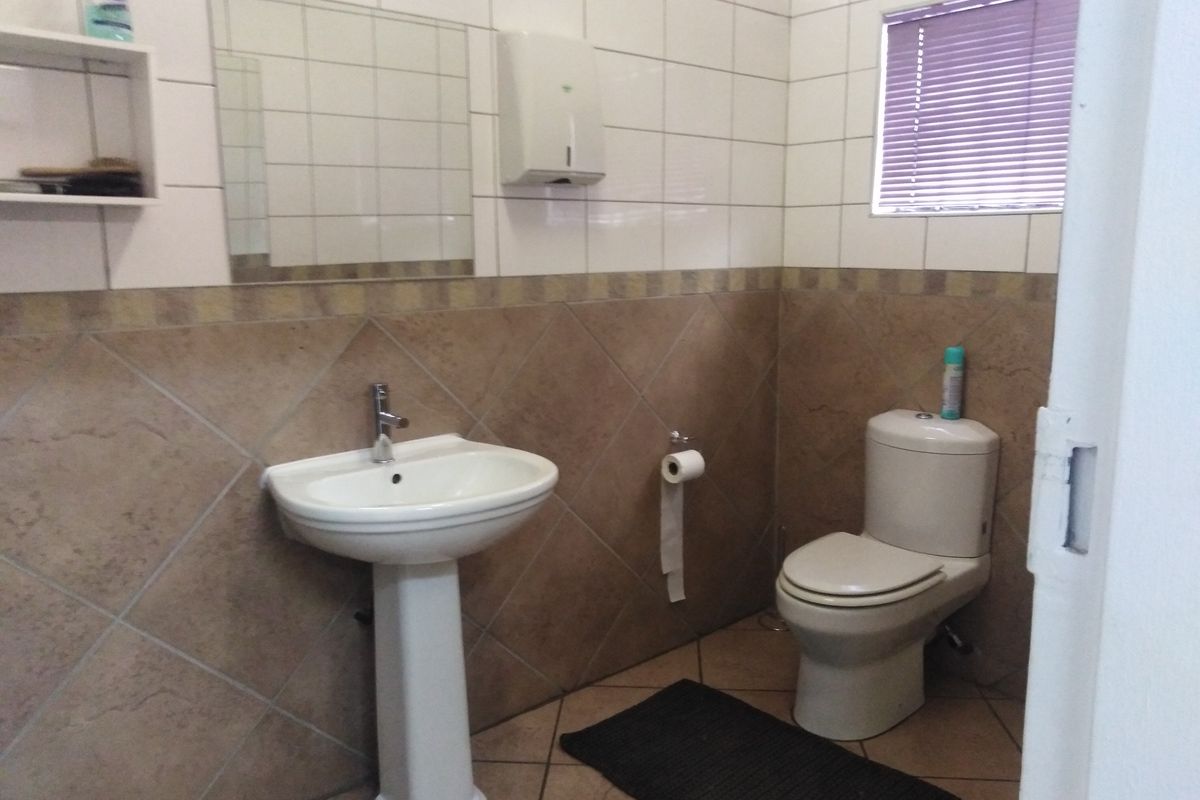A functional office bathroom featuring a pedestal washbasin, toilet, and tiled walls with a neutral color scheme.