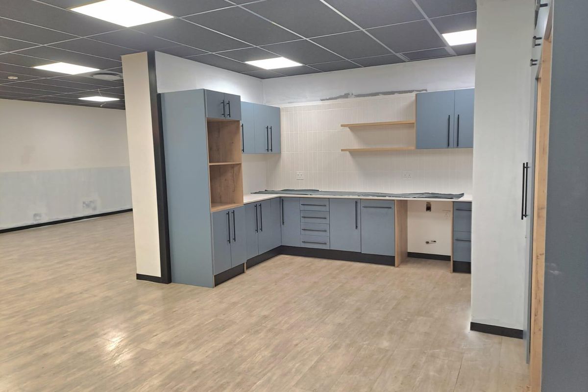 Modern office kitchenette featuring blue cabinetry, wood-look flooring, and recessed ceiling lighting in an open-plan workspace.