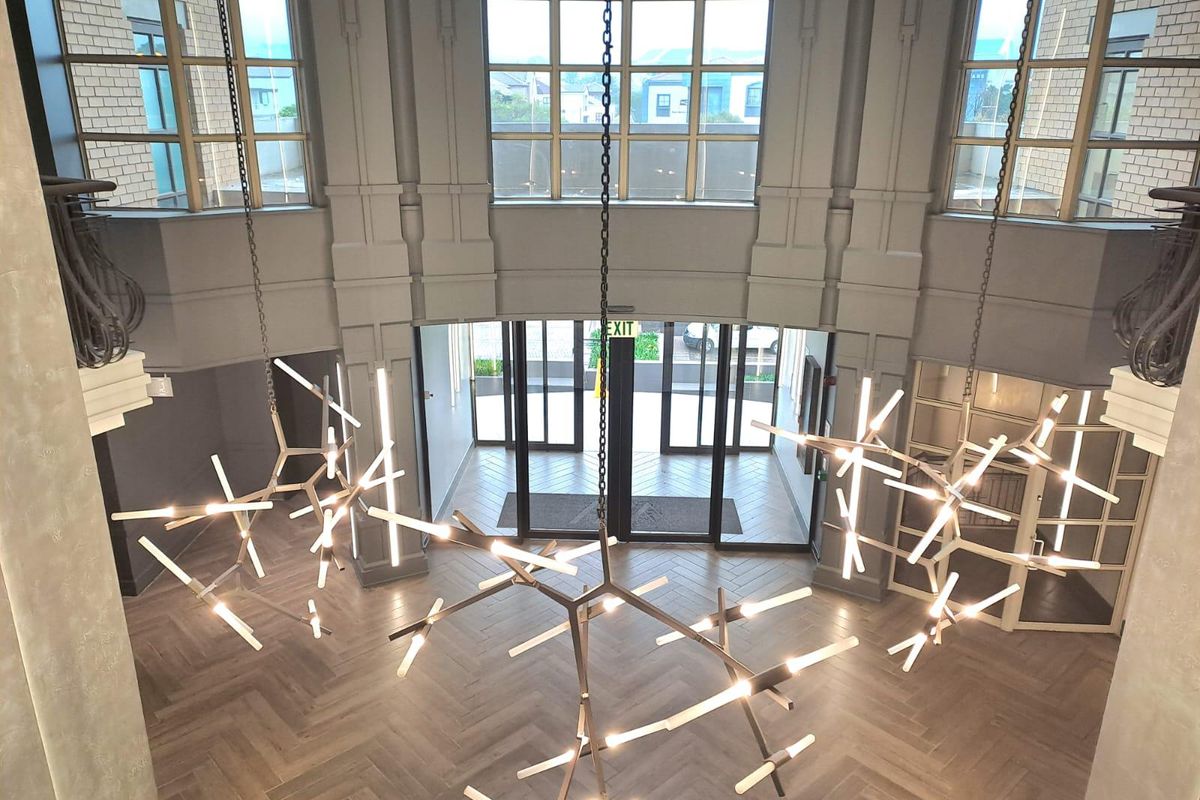 A grand, double-volume office entrance lobby featuring herringbone flooring, large glass windows, and modern statement pendant lighting.