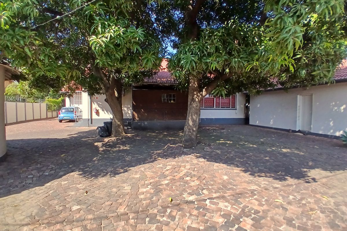 Rear exterior view of the office property featuring a large cobblestone paved courtyard area shaded by mature trees.