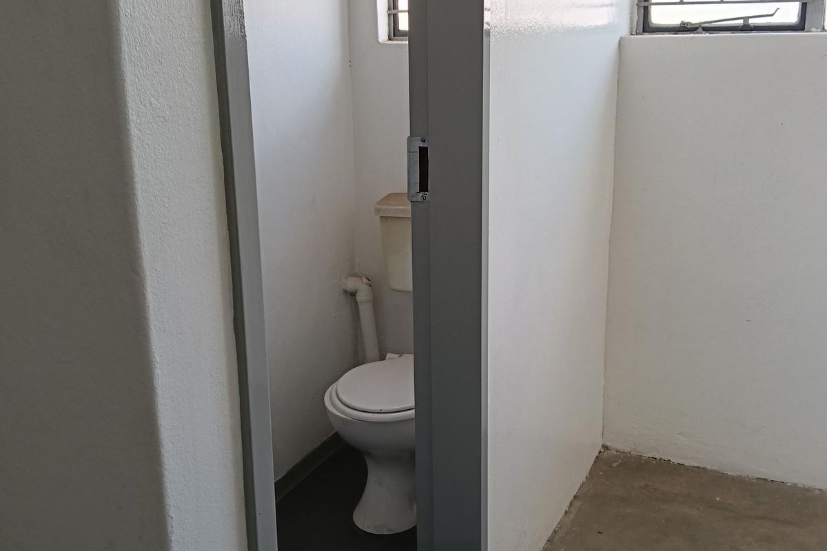 A functional industrial-style bathroom featuring a standard toilet, concrete flooring, and security bars on the windows.