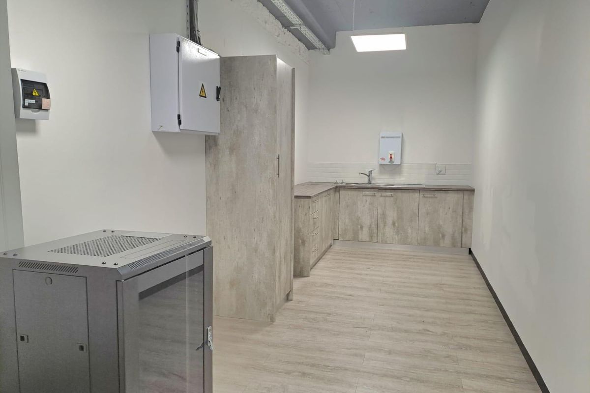 A functional office kitchenette featuring wood-look cabinetry, a stainless steel sink, and exposed industrial-style ceiling with integrated lighting.