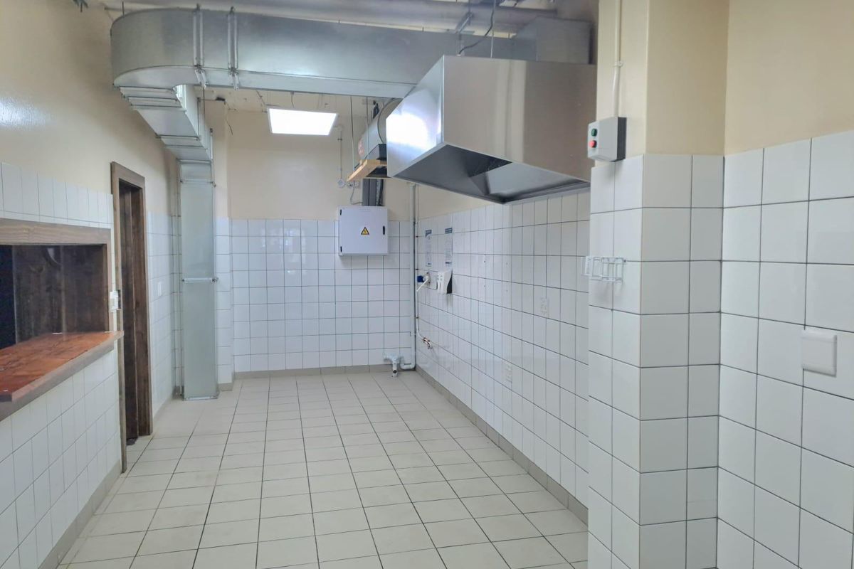 A functional commercial kitchen space featuring tiled walls, tiled flooring, and an installed stainless steel extractor hood with exposed ventilation ducting.
