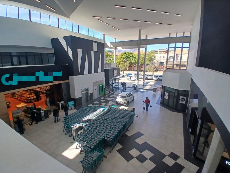 A high-ceilinged, modern commercial atrium or mall concourse featuring tiled flooring, recessed lighting, and multiple storefront access points.