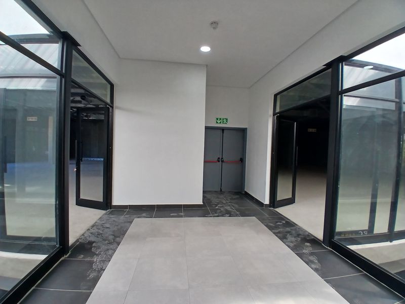 A clean, modern entrance area featuring large glass-panelled doors, tiled flooring, and a designated fire exit door.