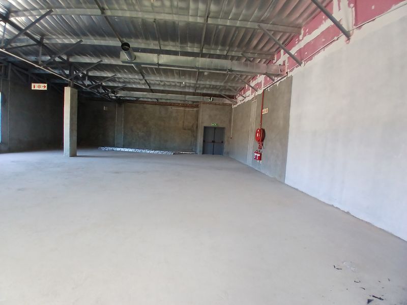 A large, open-plan commercial space featuring exposed steel roof trusses, concrete flooring, and essential fire safety equipment, currently in an unfinished shell condition.
