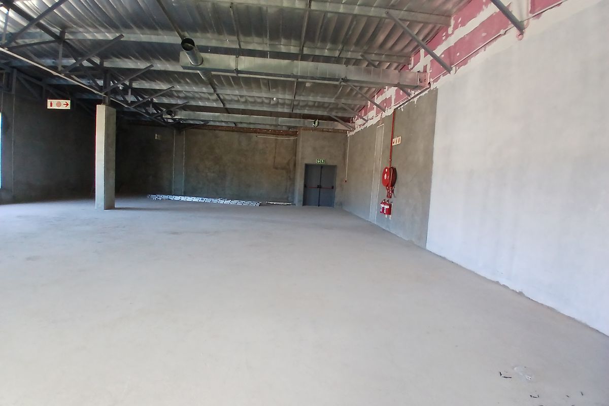 A large, open-plan commercial space featuring exposed steel roof trusses, concrete flooring, and essential fire safety equipment, currently in an unfinished shell condition.