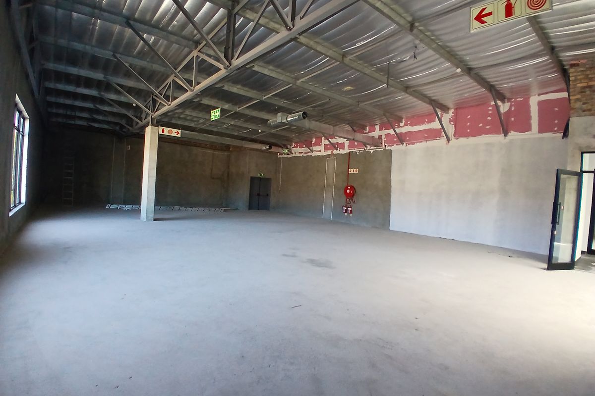 A large, open-plan commercial space featuring exposed steel roof trusses, concrete flooring, and industrial-style ventilation, currently in an unfinished shell condition.