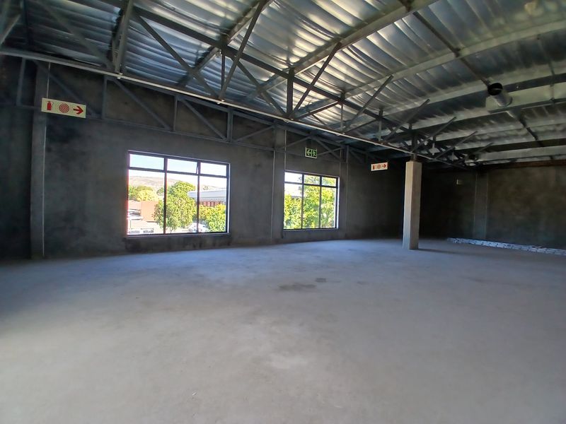A large, open-plan commercial space featuring exposed steel roof trusses, concrete flooring, and large windows, currently in an unfinished shell condition.