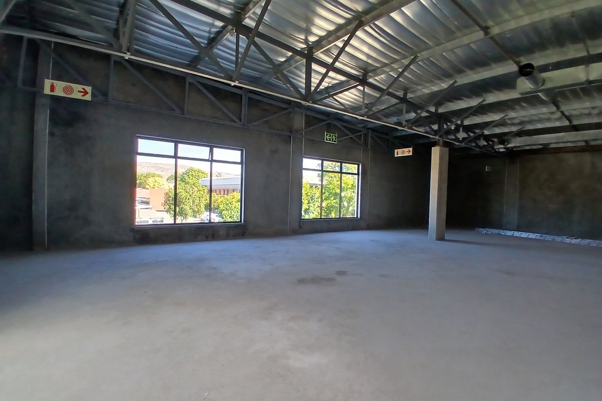 A large, open-plan commercial space featuring exposed steel roof trusses, concrete flooring, and large windows, currently in an unfinished shell condition.