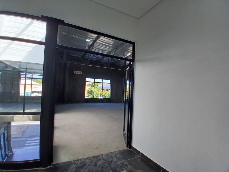 A spacious, open-plan commercial interior featuring exposed steel roof trusses, polished concrete flooring, and large black-framed windows providing ample natural light.