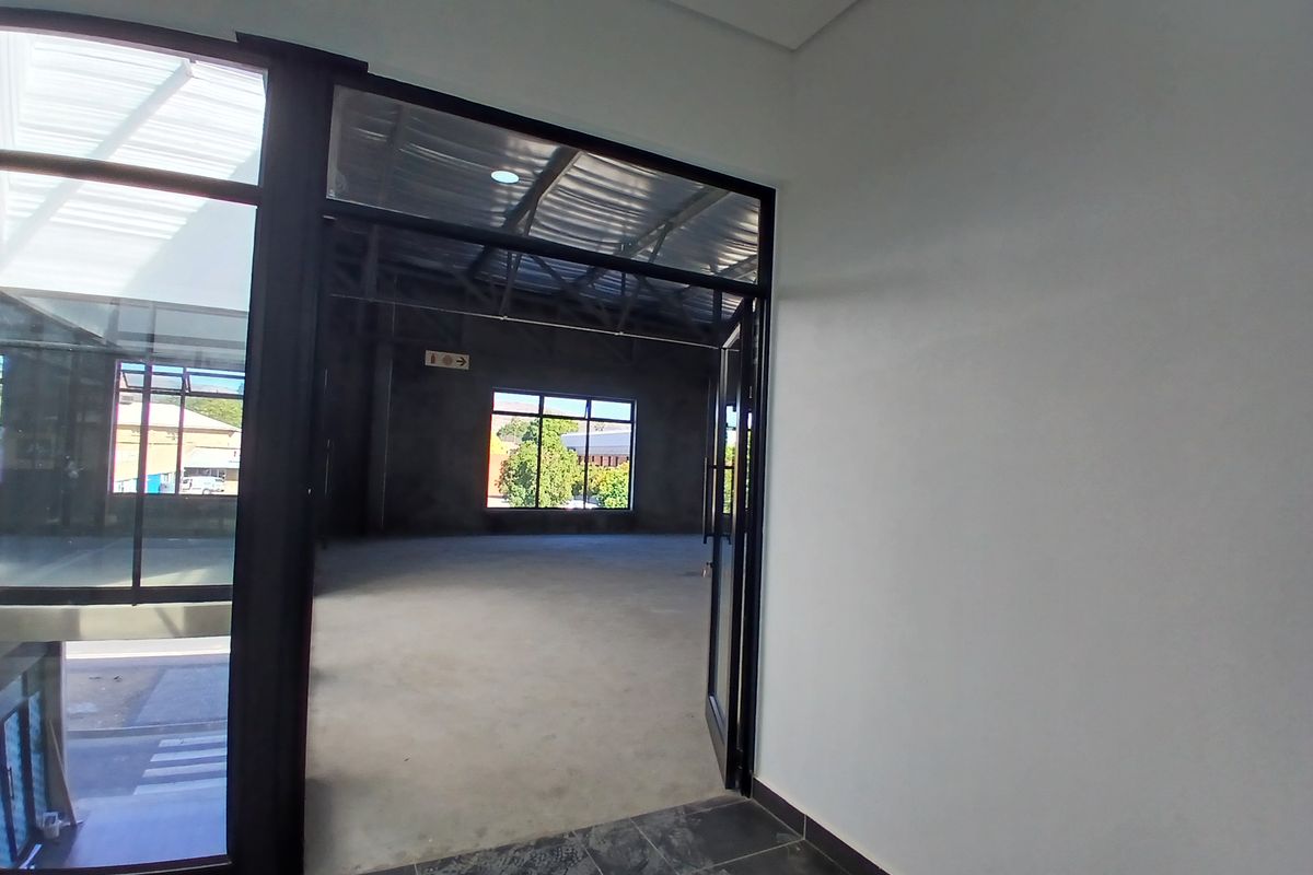 A spacious, open-plan commercial interior featuring exposed steel roof trusses, polished concrete flooring, and large black-framed windows providing ample natural light.