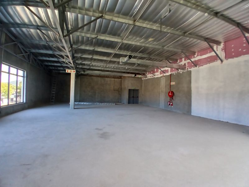 A large, open-plan commercial space featuring exposed steel roof trusses, concrete flooring, and industrial ventilation, currently in an unfinished shell condition.