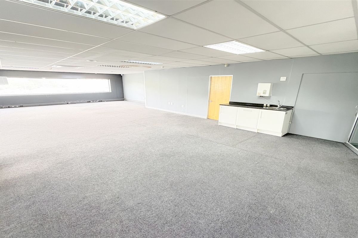 Spacious open-plan office area featuring a suspended ceiling, recessed lighting, carpeted flooring, and a convenient built-in kitchenette with a sink.