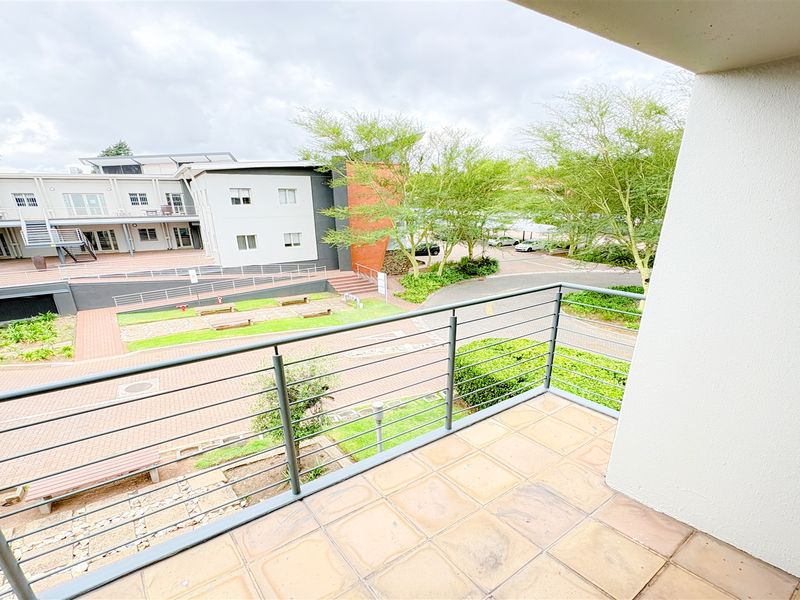 A private balcony with tiled flooring and a metal balustrade, overlooking the office park courtyard and landscaped grounds.