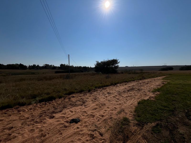 A wide-angle view of the farm landscape featuring a dirt access track, open fields, and overhead utility infrastructure under a clear sky.
