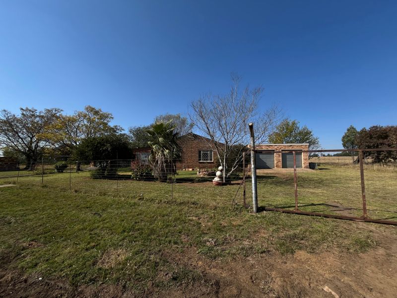 Front view of a brick farmhouse featuring a double garage, wire fencing, and a metal entrance gate on a large rural property.