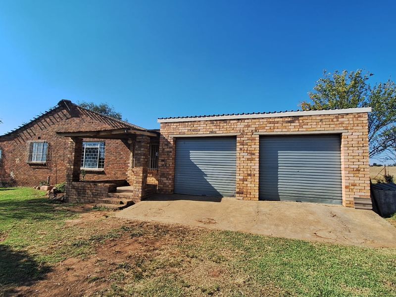 Front view of a face brick farm house featuring a double garage with roll-up doors and a covered entrance porch.