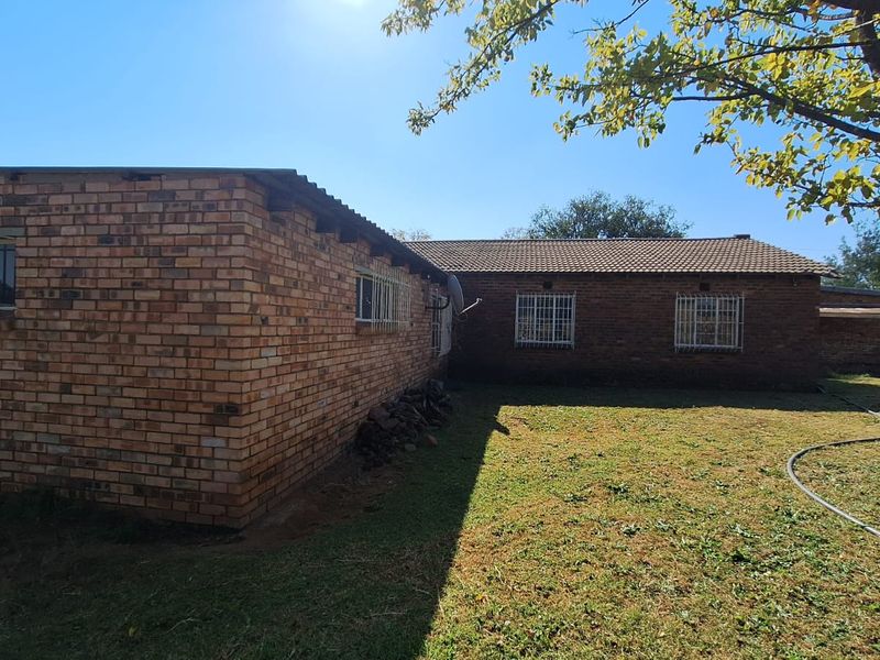 Rear view of a face brick farmhouse featuring security bars on windows and a combination of tiled and corrugated roofing set on a large lawn.