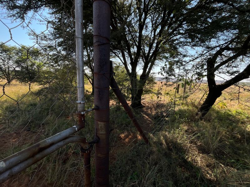 A view of the farm perimeter featuring wire mesh fencing supported by weathered and corroded metal posts set against a natural landscape.
